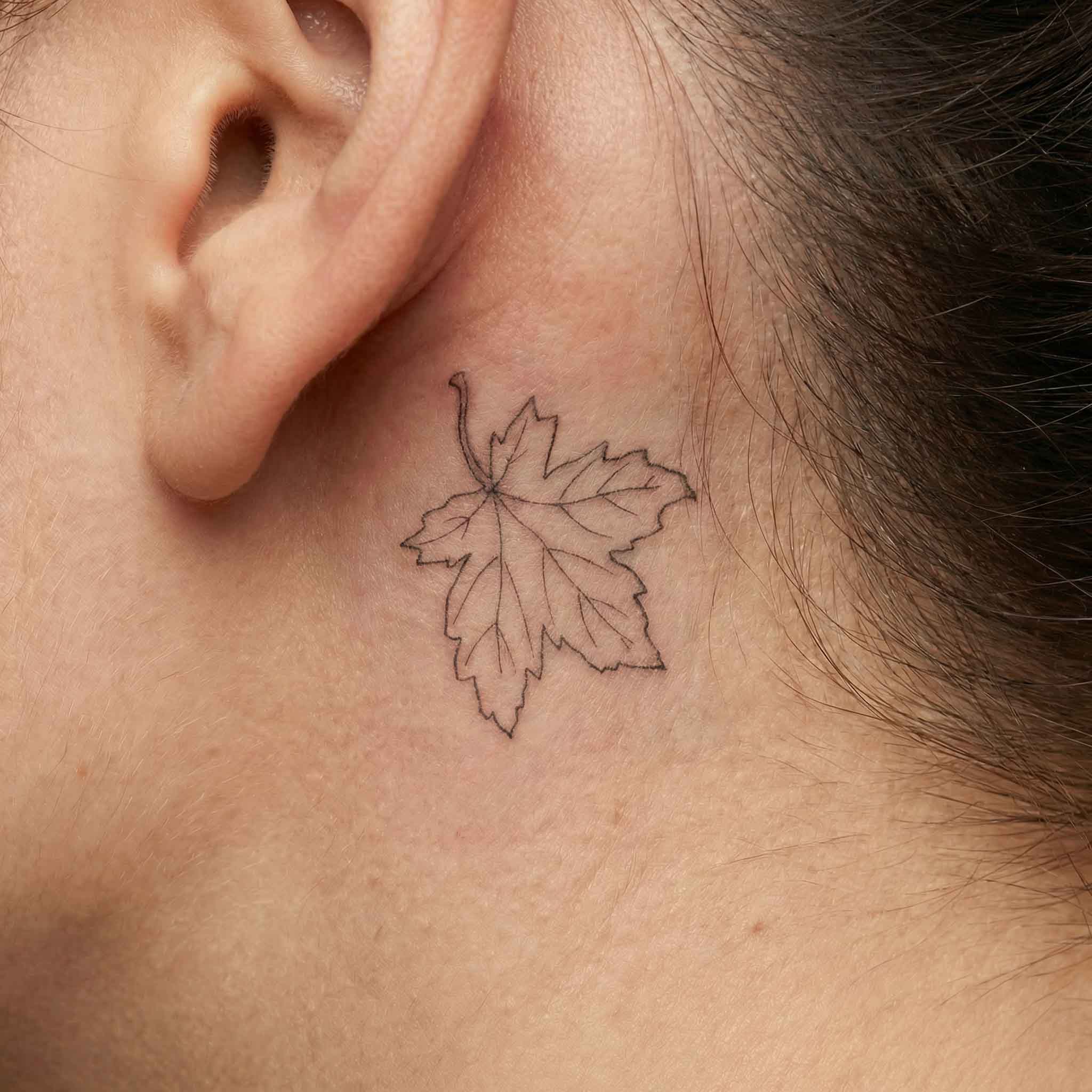 Minimal maple leaf fake tattoo worn behind the ear with delicate nature-inspired details