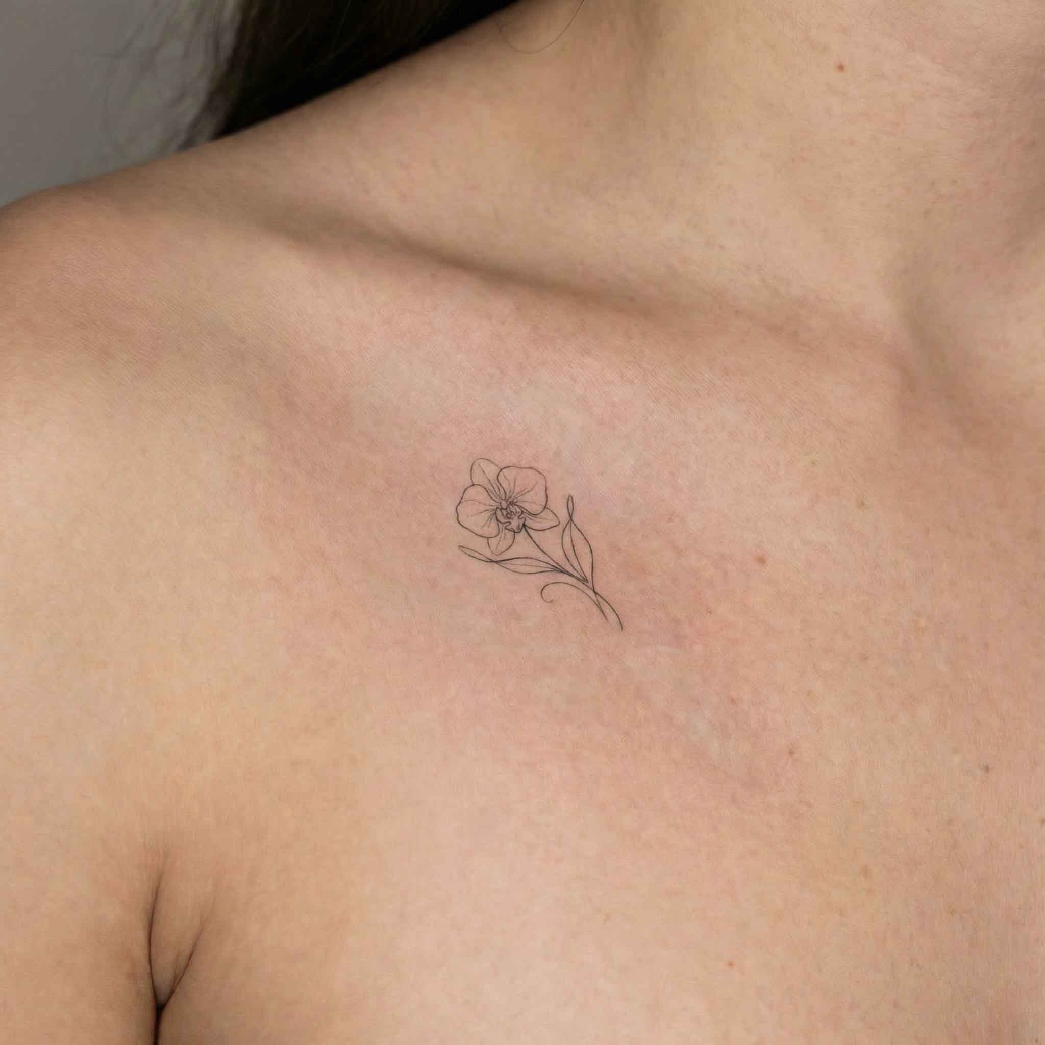 Minimal orchid tattoo worn on the collarbone with soft floral linework
