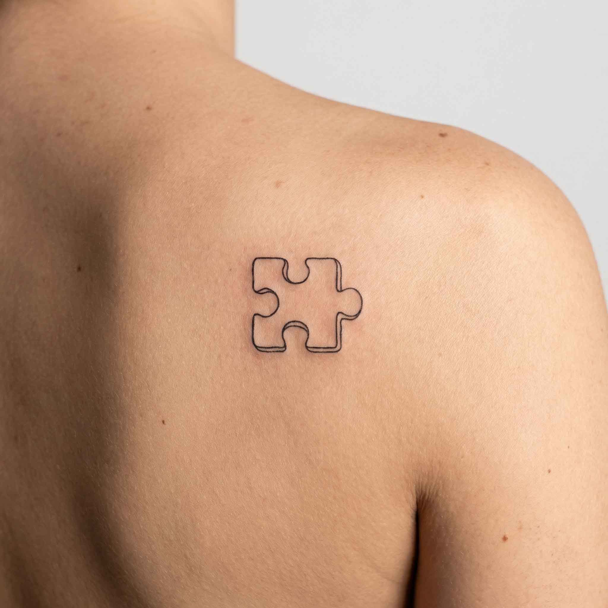 Small puzzle piece semi-permanent tattoo worn on back with minimalist symbolic style