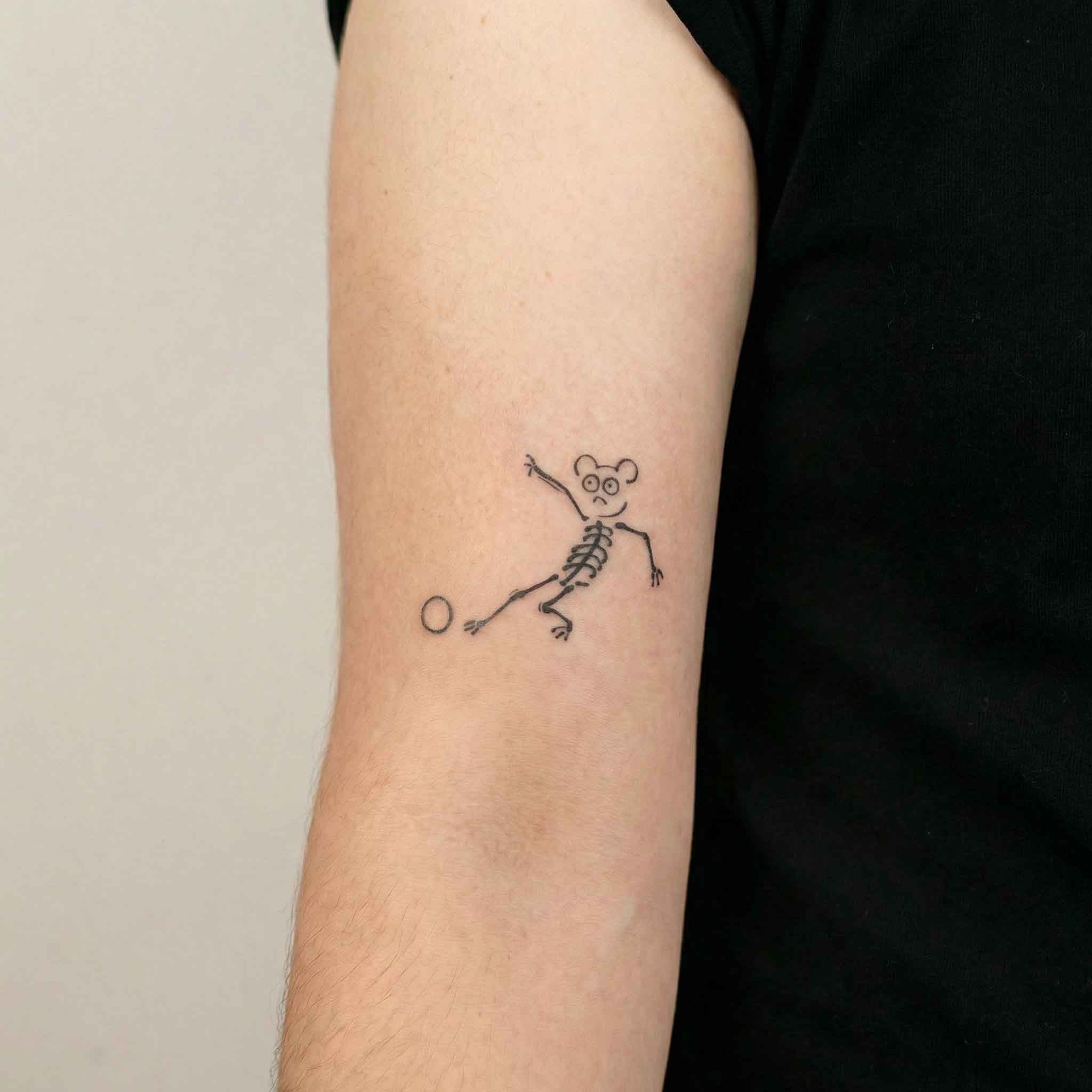 Small skeleton bear football tattoo worn on arm in minimalist style