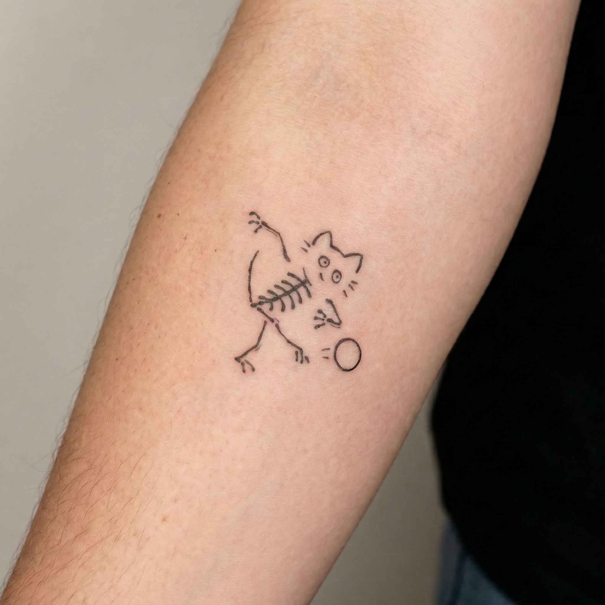 Small skeleton cat tattoo worn on arm with playful minimalist style
