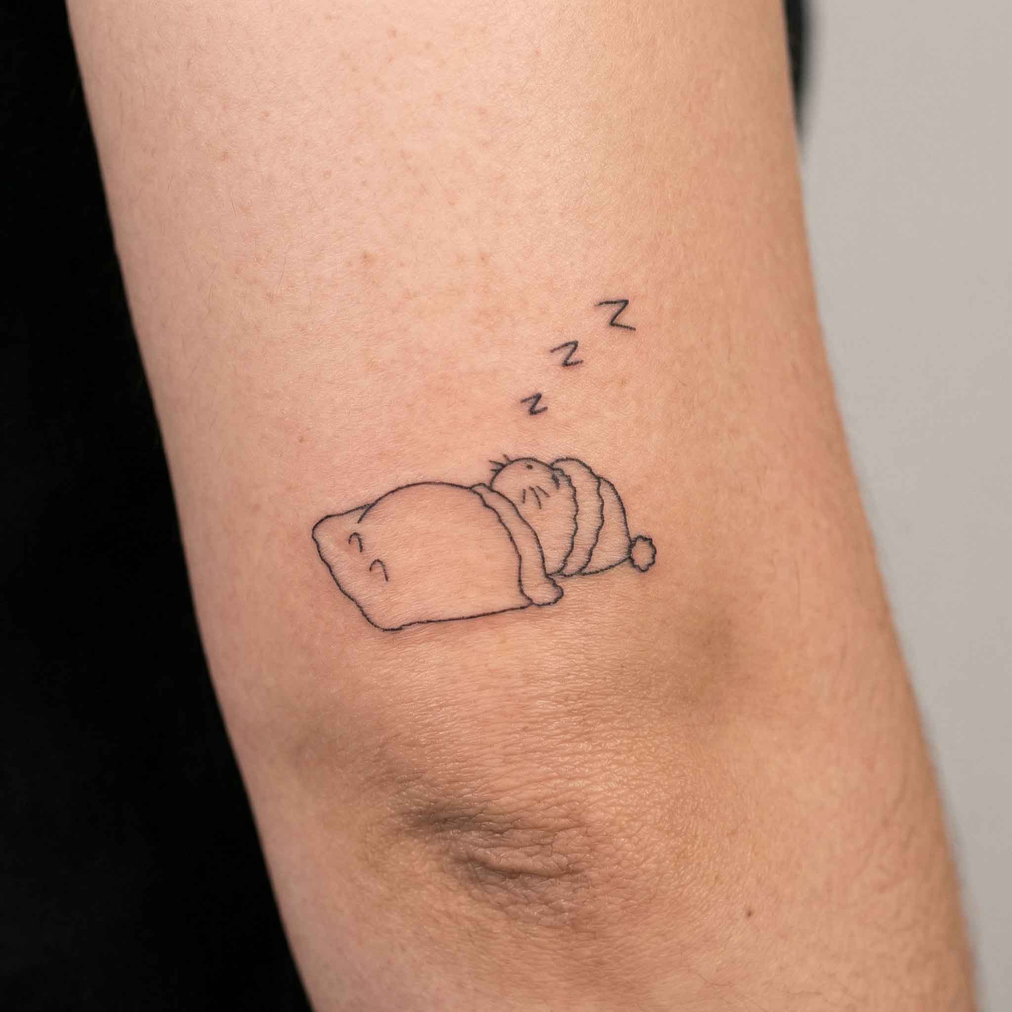 Small sleeping cat tattoo worn on arm with cozy line art