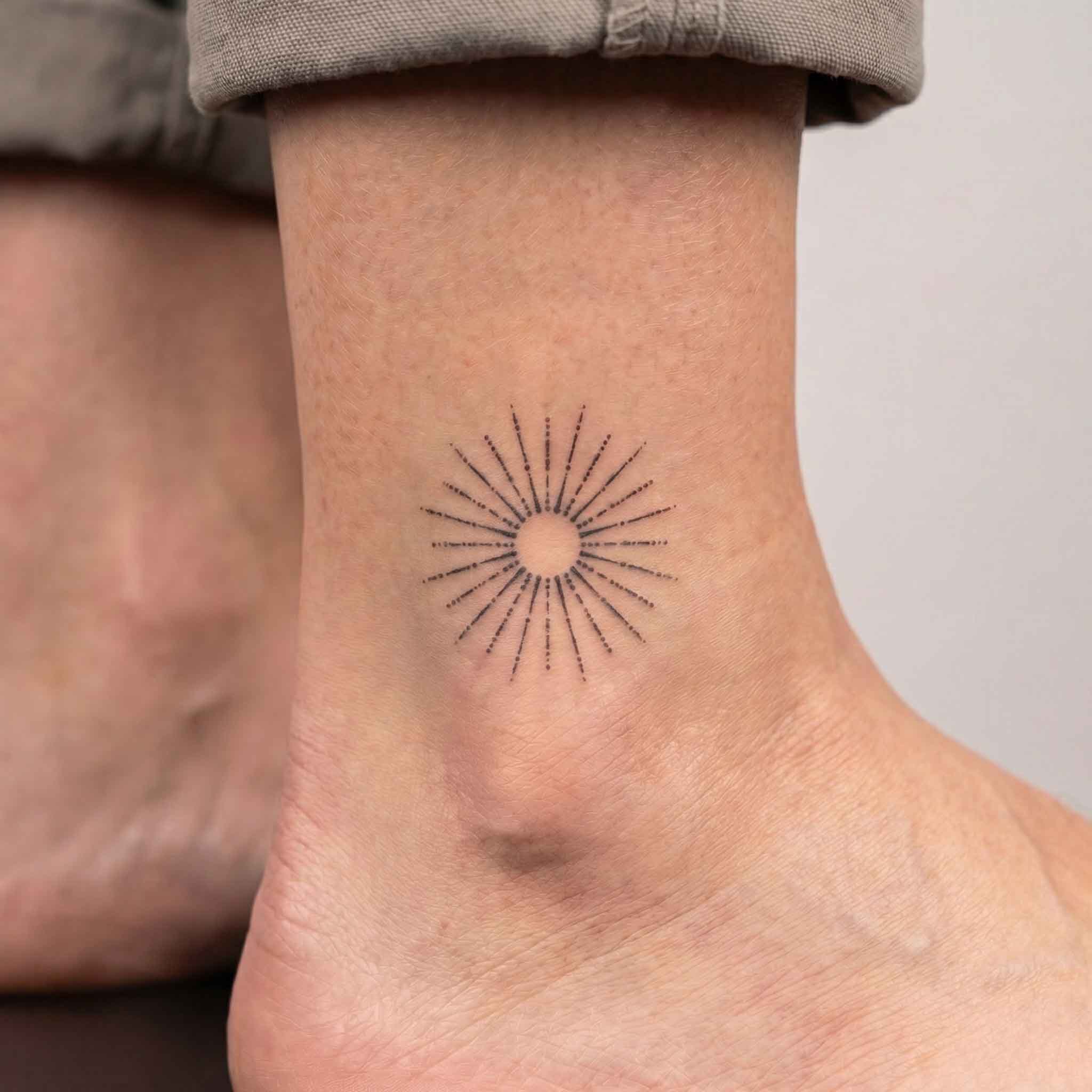 Fine line sunburst tattoo worn on ankle in minimalist geometric style