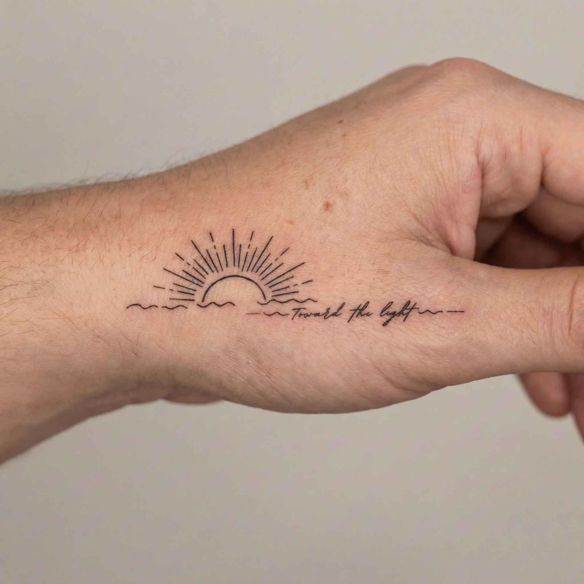 Sunrise ocean tattoo worn on the hand with simple word detail