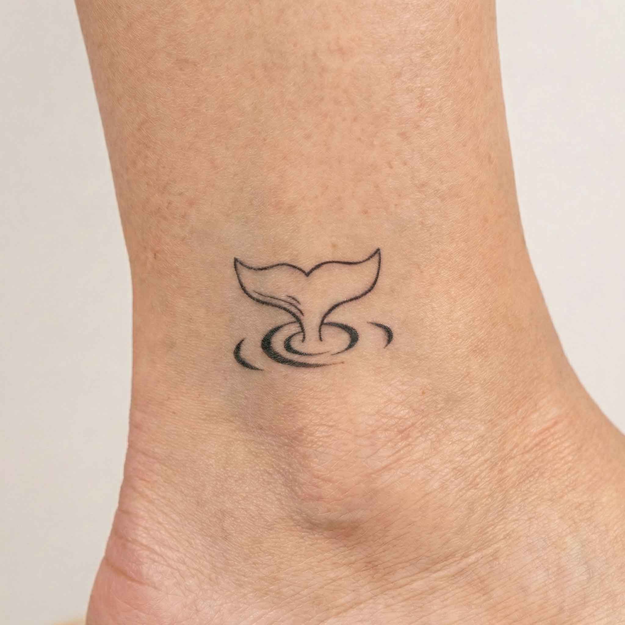 Minimal whale tail tattoo worn on the wrist with soft ocean-inspired details