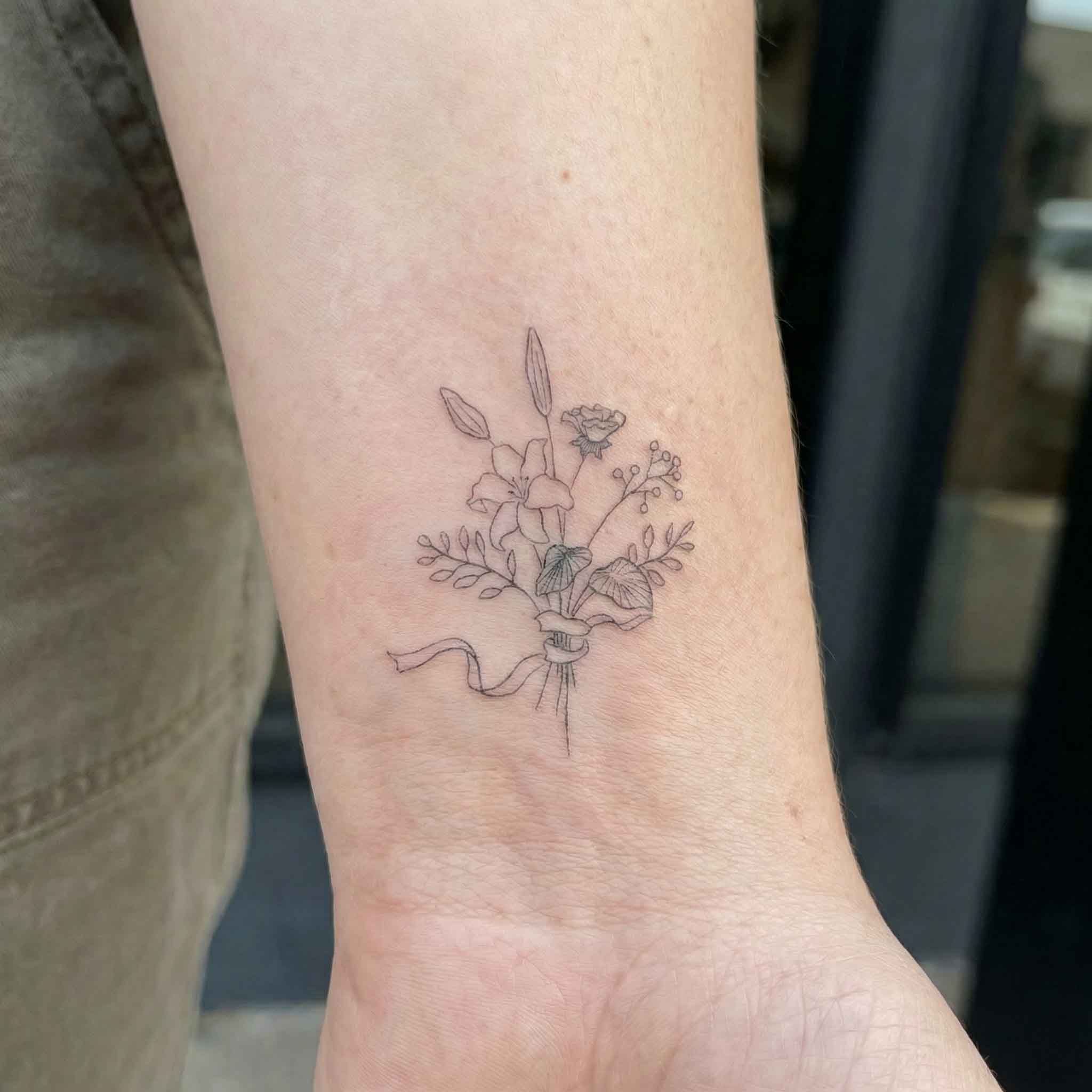 Fine line floral bouquet tattoo worn on wrist with soft botanical details